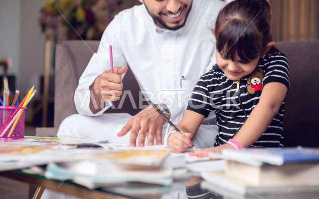 A Saudi Gulf student studying at home with her father, helping her to do her homework, distance learning, the concept of online education, home education during quarantine and the outbreak of the Corona virus, self-isolation.