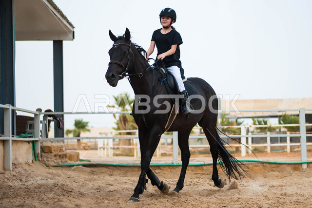  مزرعة تدريب وترويض الخيول ، ممارسة هواية ركوب الخيل ، إسطبل الأحصنة في السعودية ، أنشطة رياضية ترفيهية للأطفال في نادي الفروسية ، فتاة عربية سعودية خليجية ترتدي زي الفروسية تركب جواد أسود أصيل ، قضاء أوقات ممتعة في التدرب على ركوب الجياد