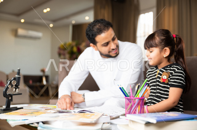 A Saudi Gulf student studying at home with her father, helping her to do her homework, distance learning, the concept of online education, home education during quarantine and the outbreak of the Corona virus, self-isolation.