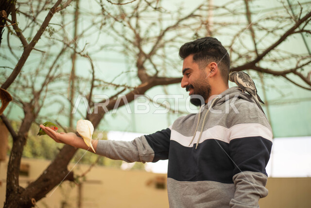 قضاء أوقات مسلية في حديقة الحيوانات، رجل عربي خليجي سعودي يطعم الطائر في محمية طيور طبيعية بالمملكة العربية السعودية ، أنشطة وفعاليات ترفيهية