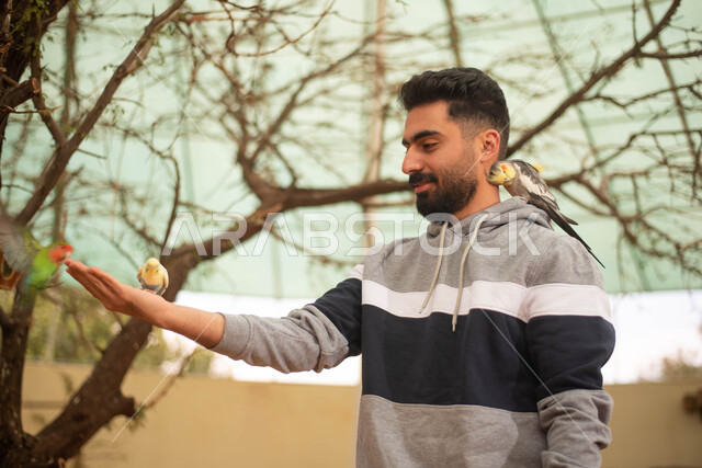 Happy face gestures, a Saudi Arabian Gulf man spending fun times in the Bird Sanctuary in the Kingdom of Saudi Arabia, entertainment activities with birds, interesting tourist places.