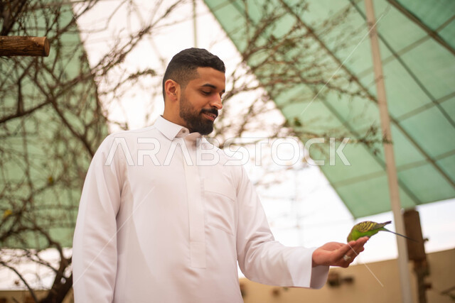 قضاء أوقات مسلية في حديقة الحيوانات، رجل عربي خليجي سعودي يمسك الطائر في محمية طيور طبيعية بالمملكة العربية السعودية ، أنشطة وفعاليات ترفيهية