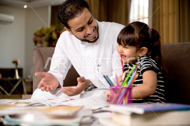 A Saudi Gulf student studying at home with her father, helping her to do her homework, distance learning, the concept of online education, home education during quarantine and the outbreak of the Corona virus, self-isolation.