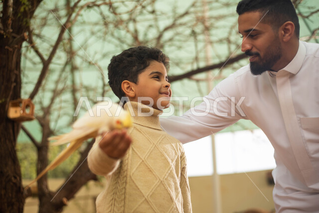 تربية الطيور في المحمية الطبيعية، أنشطة ترفيهية في فعالية سفاري موسم الرياض، رجل عربي خليجي سعودي وابنه يمرحان مع الطيور في حديقة الحيوانات في المملكة العربية السعودية .