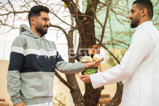 فعاليات ترفيهية في موسم سفاري الرياض، تربية ورعاية الحيوانات، ايماءات وجه تدل على الاستمتاع مع الصديق، صورة مقربة لرجلين عربيين خليجيين سعوديين يقضيان أوقات مسلية مع الطيور في محمية طبيعية في المملكة العربية السعودية.