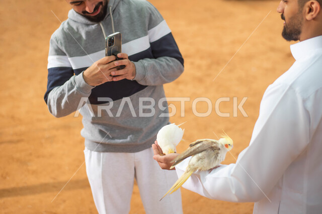 Taking souvenir photos, two Saudi Arabian Gulf men in a nature reserve in the Kingdom of Saudi Arabia, using a mobile phone, recreational activities with birds, the Riyadh Season safari event.