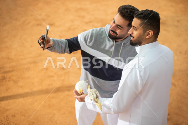 التقاط  صور تذكارية ، رجلان عربيان خليجيان سعوديان في محمية طبيعية في المملكة العربية السعودية، استخدام الهاتف المحمول ، أنشطة ترفيهية مع الطيور ، فعالية سفاري موسم الرياض.