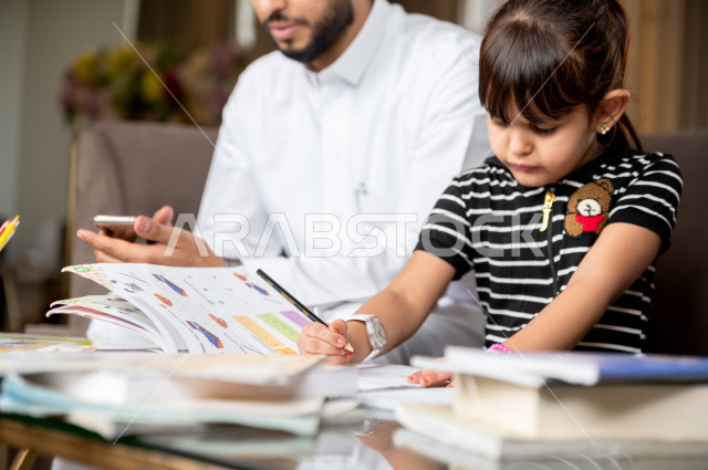 تلميذة سعودية خليجية تدرس في المنزل مع والدها ، يساعدها على تأدية واجباتها المدرسية ، التعلم عن بعد ، مفهوم التعليم عبر الانترنت ، التعليم المنزلي اثناء الحجر الصحي و تفشي فيروس كورونا ، العزلة الذاتية .