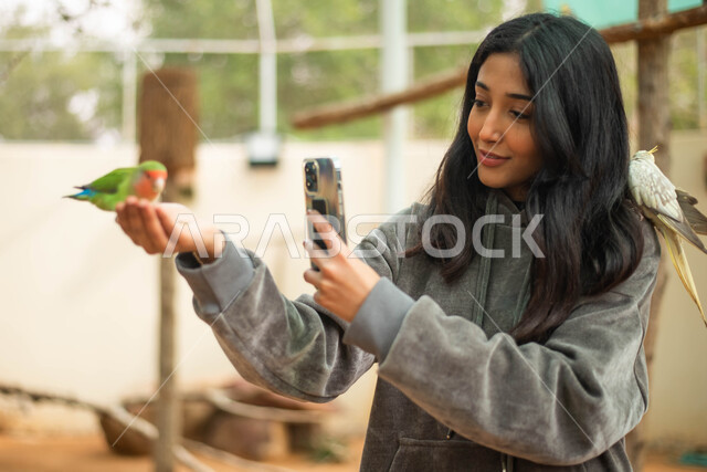 طيور في المحمية الطبيعية، استخدام الهاتف المحمول ، فتاة عربية خليجية سعودية تلتقط الصور لطائر في حديقة الحيوانات في المملكة العربية السعودية ،  مزارع تربية الطيور، أماكن سياحية ترفيهية.