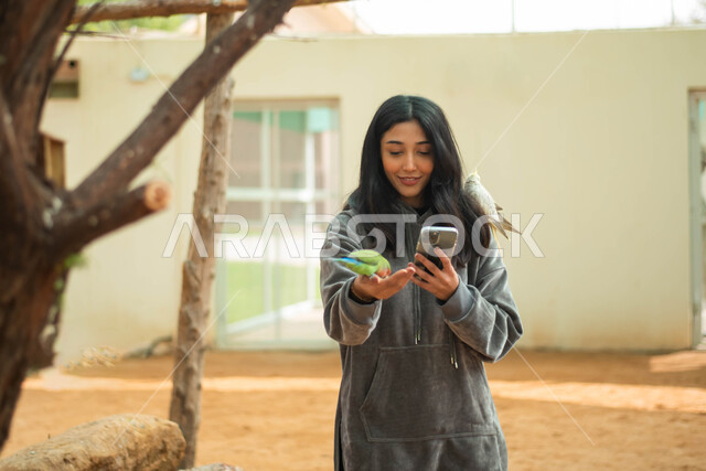 موهبة التصوير، التقاط الصور التذكارية باستخدام الهاتف المحمول، فتاة عربية خليجية سعودية تمضي اوقات ممتعة في حديقة الحيوانات ، أنشطة ترفيهية مع الطيور ، فعالية سفاري موسم الرياض.
