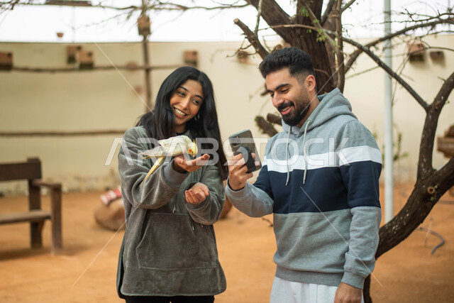 ايماءات تدل على السعادة، أنشطة ترفيهية، زوجان عربيان خليجيان سعوديان في محمية الطيور في حديقة الحيوانات في السعودية ، استخدام الهاتف المحمول، التقاط  صور تذكارية، فعالية سفاري موسم الرياض.