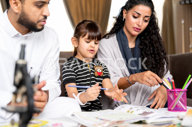 تلميذة سعودية خليجية تدرس في المنزل مع والدها و والدتها ، يساعدانها على تأدية واجباتها المدرسية ، التعلم عن بعد ، مفهوم التعليم عبر الانترنت ، التعليم المنزلي اثناء الحجر الصحي و تفشي فيروس كورونا ، العزلة الذاتية .