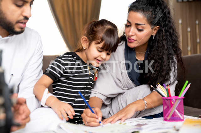 تلميذة سعودية خليجية تدرس في المنزل مع والدها و والدتها ، يساعدانها على تأدية واجباتها المدرسية ، التعلم عن بعد ، مفهوم التعليم عبر الانترنت ، التعليم المنزلي اثناء الحجر الصحي و تفشي فيروس كورونا ، العزلة الذاتية .