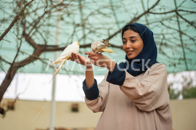 Enjoying and having fun with birds, a summer holiday and a happy atmosphere, a close-up of a Saudi Arabian Gulf woman in the zoo in the Kingdom of Saudi Arabia, recreational tourist places, birds in the nature reserve.