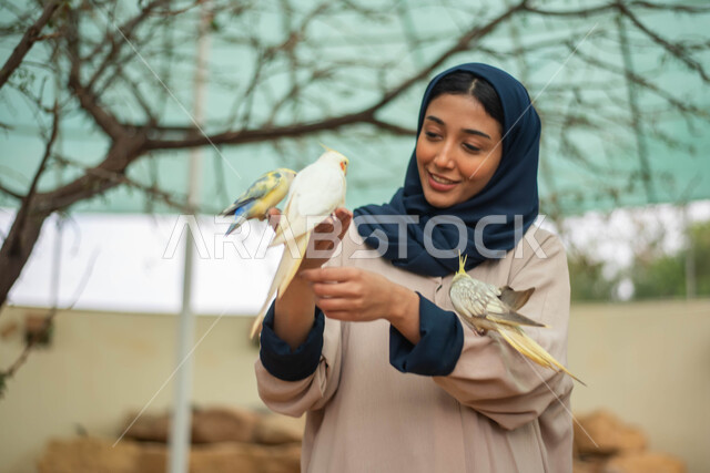 خلفية الطبيعة، إيماءات وجه تدل على السعادة والاستمتاع باللهو مع الطيور، أماكن سياحية وفعاليات ترفيهية بالسعودية، صورة مقربة لامرأة عربية خليجية سعودية محجبة في حديقة الحيوانات في المملكة العربية السعودية، محمية طبيعية.