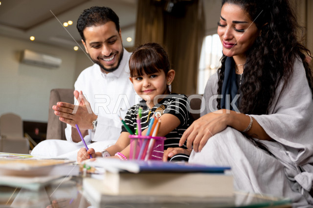 تلميذة سعودية خليجية تدرس في المنزل مع والدها و والدتها ، يساعدانها على تأدية واجباتها المدرسية ، التعلم عن بعد ، مفهوم التعليم عبر الانترنت ، التعليم المنزلي اثناء الحجر الصحي و تفشي فيروس كورونا ، العزلة الذاتية .