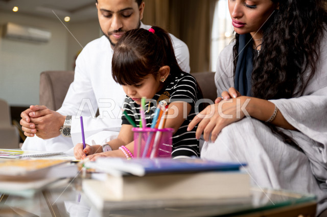 تلميذة سعودية خليجية تدرس في المنزل مع والدها و والدتها ، يساعدانها على تأدية واجباتها المدرسية ، التعلم عن بعد ، مفهوم التعليم عبر الانترنت ، التعليم المنزلي اثناء الحجر الصحي و تفشي فيروس كورونا ، العزلة الذاتية .