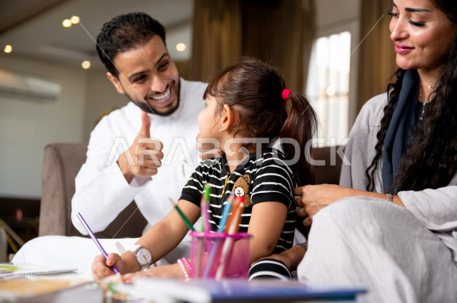 تلميذة سعودية خليجية تدرس في المنزل مع والدها و والدتها ، يساعدانها على تأدية واجباتها المدرسية ، التعلم عن بعد ، مفهوم التعليم عبر الانترنت ، التعليم المنزلي اثناء الحجر الصحي و تفشي فيروس كورونا ، العزلة الذاتية .