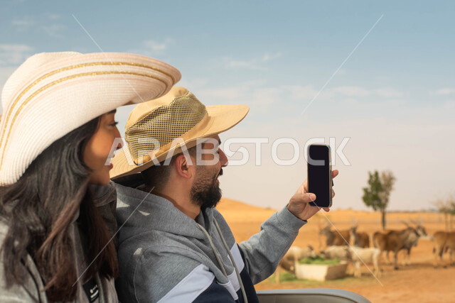 التقاط صور تذكارية لتوثيق اللحظات الجميلة,  زوجان عربيان خليجيان سعوديان يقومان بجولة سياحية في حديقة الحيوانات في المملكة العربية السعودية, ايماءات وجه تدل على السعادة و الاستمتاع, أوقات ممتعة و فعاليات ترفيهية عائلية في سفاري الرياض.