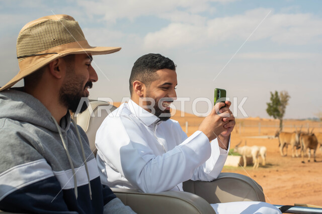 التقاط صور تذكارية لتوثيق اللحظات الجميلة,  شابان عربيان خليجيان سعوديان يقومان بجولة سياحية في حديقة الحيوانات في المملكة العربية السعودية, ايماءات وجه تدل على السعادة و الاستمتاع برفقة الأصدقاء, أوقات ممتعة و فعاليات ترفيهية عائلية في سفاري الرياض.