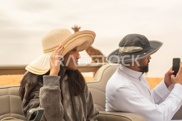 توثيق اللحظات و التقاط صور بإستخدام الهاتف المحمول, زوجان عربيان خليجيان سعوديان يقومان بجولة سياحية في حديقة الحيوانات في المملكة العربية السعودية, ايماءات وجه تدل على السعادة و الاستمتاع, أوقات ممتعة و فعاليات ترفيهية عائلية في سفاري الرياض.