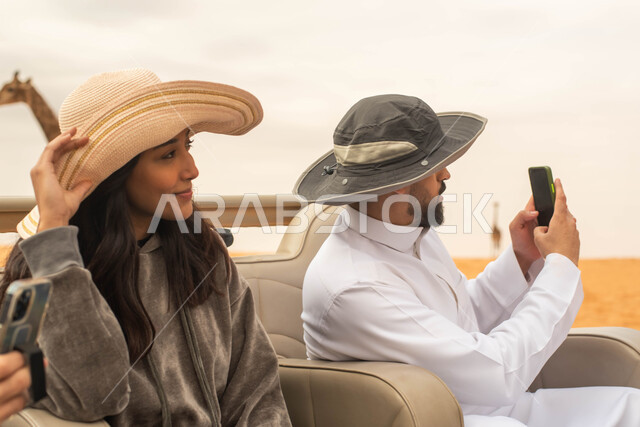 Taking pictures using a mobile phone, a Saudi Arabian Gulf couple taking a tour in the zoo in the Kingdom of Saudi Arabia, facial gestures indicating happiness and enjoyment, fun times and family entertainment activities in the Riyadh safari.
