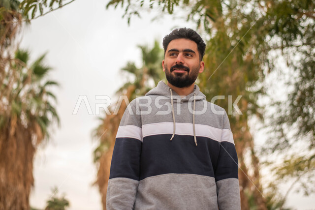 ايماءات وجه تدل على السعادة و السرور, صورة مقربة لشاب عربي خليجي سعودي مبتسم يتجول في إحدى الحدائق العامة، قضاء أوقات ممتعة، التجول و المشي في الهواء الطلق في حدائق ومنتزهات المملكة العربية السعودية.