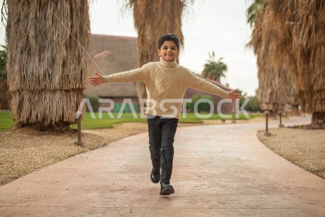 اللهو و اللعب, طفل عربي خليجي سعودي يركض في إحدى الحدائق العامة، قضاء أوقات ممتعة في العطلة الصيفية، ايماءات وجه تدل على السعادة و السرور، نزهه في الهواء الطلق في حدائق ومنتزهات المملكة العربية السعودية, صورة الجسم بالطول الكامل.