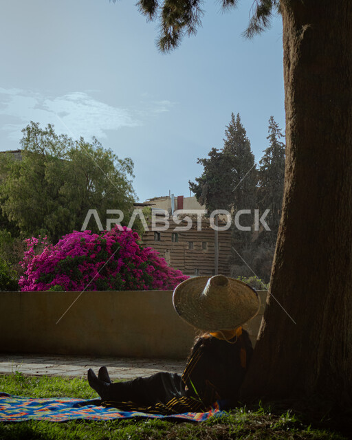 الاشجار والنباتات الخضراء في الاماكن الاثرية في مدينة عسير في المملكة العربية السعودية، زراعة الورود والازهار الطبيعية، فتاة عربية خليجية سعودية ترتدي الازياء الشعبية الجنوبية وتجلس تحت الشجرة، مناظر طبيعية من المنطقة الجنوبية في المملكة العربية السعودية