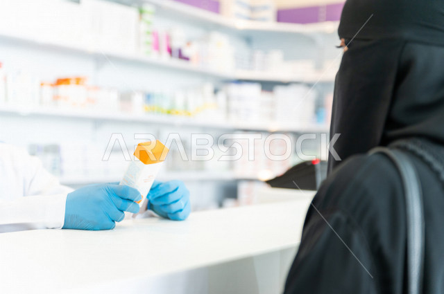 سيدة عربية خليجية سعودية تقوم بطلب الادوية من صيدلي خليجي يرتدي الكمامة للوقاية من فايروس كورونا ، اختيار الادوية والمنتجات الطبية ،شراء الادوية الموجودة في الوصفات الطبية  ، الاستفادة من الخدمات والرعاية الصحية 