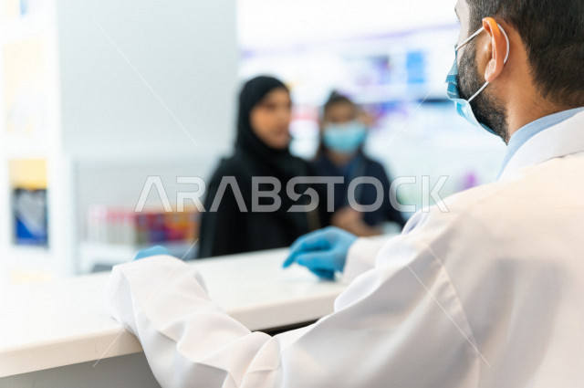 سيدة عربية خليجية سعودية تقوم بطلب الادوية من صيدلي خليجي يرتدي الكمامة للوقاية من فايروس كورونا ، اختيار الادوية والمنتجات الطبية ،شراء الادوية الموجودة في الوصفات الطبية  ، الاستفادة من الخدمات والرعاية الصحية 