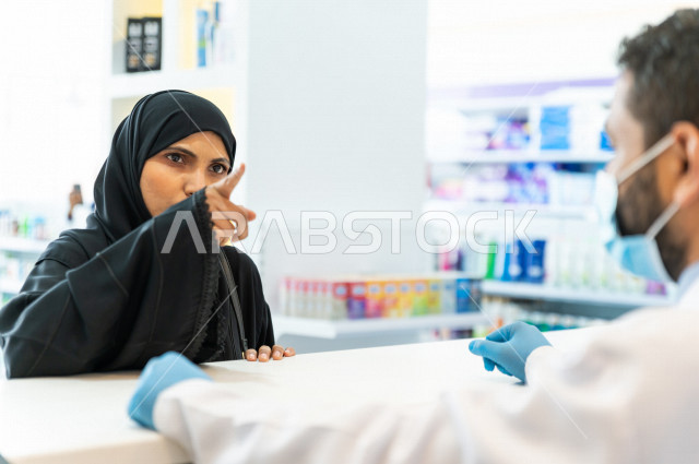 سيدة عربية خليجية سعودية تقوم بطلب الادوية من صيدلي خليجي يرتدي الكمامة للوقاية من فايروس كورونا ، اختيار الادوية والمنتجات الطبية ،شراء الادوية الموجودة في الوصفات الطبية  ، الاستفادة من الخدمات والرعاية الصحية 