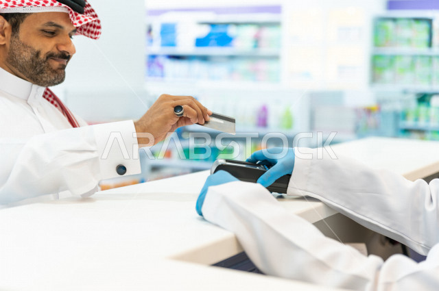 رجل عربي خليجي سعودي داخل الصيدلية ، يقوم بدفع ثمن الادوية من خلال البطاقة الائتمانية ، شراء الادوية والمستلزمات الطبية ،طلب الادوية الموجودة في الوصفة الطبية ، الاستفادة من الخدمات الصحية