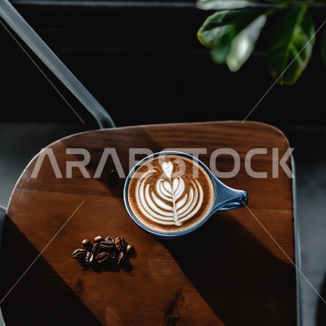 مشروبات ساخنة لذيذة ، صورة من الاعلى  لكوب من القهوه برغوة كثيفة مع رسومات على طاولة خشبية ، حبات البن الطازجة, مشروب الكابتشينو الساخن ، قهوة اسبرسو, كافيهات ومطاعم في السعودية