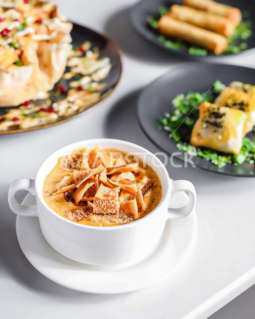 صورة مقربة لمائدة طعام بأصناف متنوعة ,طبق مقبلات ساخنة لذيذ ، شوربة العدس الصحية و الشهية و اللذيذة المزينة بقطع الخبز المقرمش ،مطاعم عربية خليجية سعودية , خلفية بيضاء .