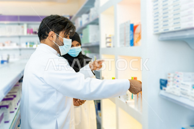 رجل وامراة عربيان خليجيان سعوديان يرتديان الكمامة للوقاية من فايروس كورونا ،  يقومان بجرد الادوية داخل الصيدلية ، مناقشة امور خاصة بالعمل ، فحص مخزون الأدوية ، تقديم الرعاية الصحية بجودة عالية ، الادوية والمستلزمات الطبية ، مهنة الصيدلة