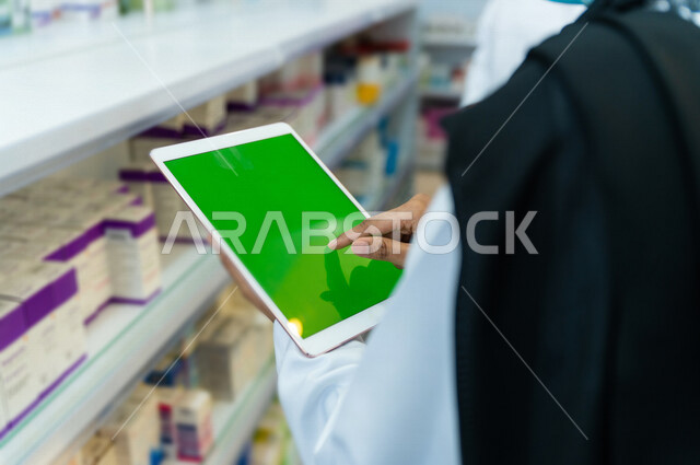صيدلي عربي خليجي سعودية يحمل بيده جهاز التابلت بشاشة كروما الخضراء  ، فحص مخزون الادوية ، عرض الادوية والمنتجات الطبية ، بيع الادوية اونلاين ، الاعلان والتسويق للمستلزمات الطبية ، مهنة الصيدلة 
