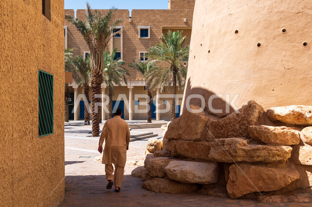 معالم الرياض التاريخية، صورة من الخلف لرجل سائح يتجول في الزقاق المحيطة بقصر المصمك التاريخي في مدينة الرياض في السعودية، الهندسة المعمارية القديمة، اماكن اثرية تراثية سياحية في السعودية