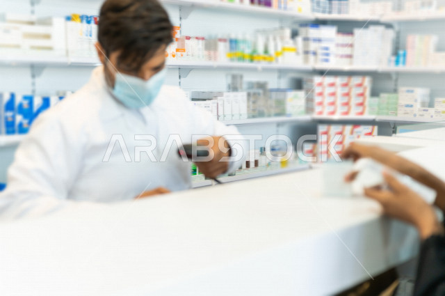 صيدلي عربي سعودي خليجي يرتدي الكمامة للوقاية من فايروس كورونا ، يحمل بيده الدواء للمريض ، صرف الادوية الموجودة في الوصفات الطبية ، توفير وتجهيز الادوية اللازمة ، بيع الادوية والمستلزمات الطبية ، مهنة الصيدلة
