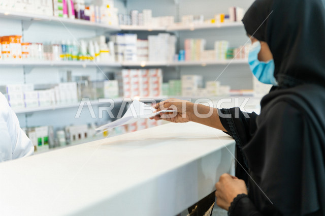  سيدة عربية خليجية سعودية تقوم بتقديم الوصفة الطبية لصيدلي خليجي سعودي ، ارتداء الكمامة الطبية للوقاية من فايروس كورونا ،صرف الادوية الموجودة في الوصفات الطبية ، توفير وتجهيز الادوية اللازمة للمريضة ، بيع الادوية والمستلزمات الطبية ، مهنة الصيدلة