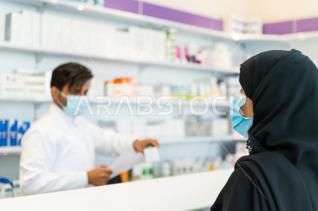  سيدة عربية خليجية سعودية تقوم بتقديم الوصفة الطبية لصيدلي خليجي سعودي ، ارتداء الكمامة الطبية للوقاية من فايروس كورونا ،صرف الادوية الموجودة في الوصفات الطبية ، توفير وتجهيز الادوية اللازمة للمريضة ، بيع الادوية والمستلزمات الطبية ، مهنة الصيدلة