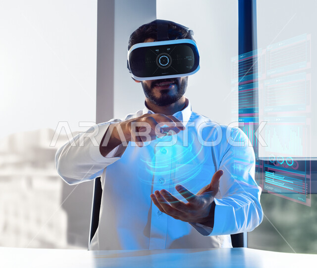 امساك واحتواء عنصر هولوجرامي، رجل عربي خليجي سعودي يرتدي نظارات الواقع الافتراضي ثلاثية الابعاد ويحمل شئ بين يديه بالواقع الإفتراضي، الاستمتاع والتفاعل ومحاكاة العالم الافتراضي، حركة يد واشارات