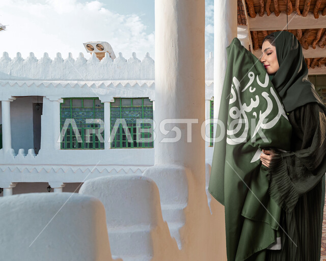 الاحتفال بيوم العلم السعودي، ذكرى اليوم الوطني السعودي، إمرأة سعودية خليجية عربية محجبة ترتدي ازياء تراثية للمناسبات الوطنية والاحتفالية وتمسك علم المملكة العربية السعودية داخل قصر المربع، عيد وطني سعودي، معالم اثرية تاريخية قديمة، قصور الرياض