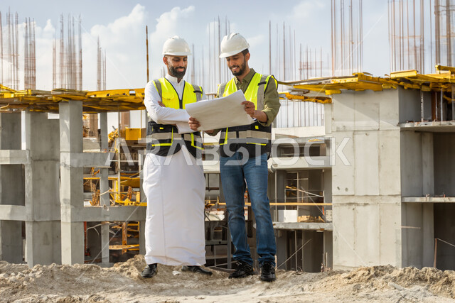 حوارات ونقاشات عمل، العمل في موقع البناء، مهندسان معماريان عربيان سعوديان خليجيان يتناقشان في ورقة مخطط البناء، ارتداء خوذة وسترة الحماية الخاصة بالعمل، التدقيق والاشراف على العمل