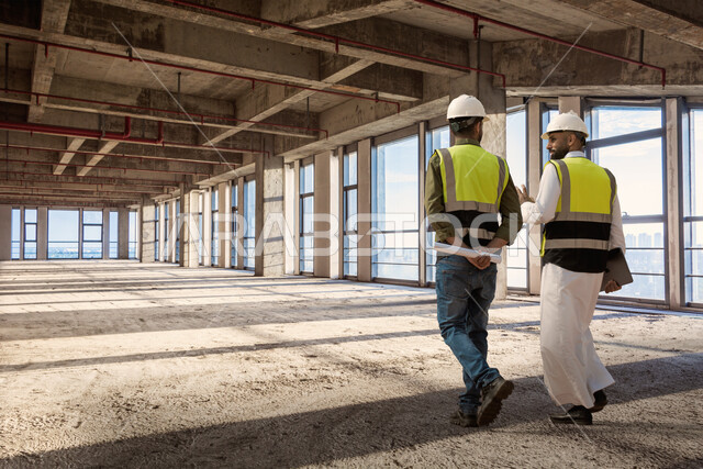 التدقيق والاشراف على العمل، ارتداء خوذة وسترة الحماية الخاصة بالعمل، مهندسان معماريان عربيان سعوديان خليجيان يتجولان في موقع البناء، حوارات ونقاشات عمل