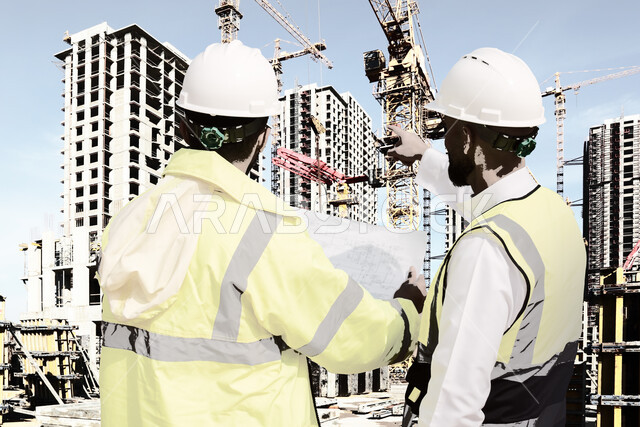 العمل في موقع البناء، مهندسان معماريان عربيان سعوديان خليجيان يتناقشان في ورقة مخطط البناء، ارتداء خوذة وسترة الحماية الخاصة بالعمل، حوارات ونقاشات عمل، التدقيق والاشراف على العمل