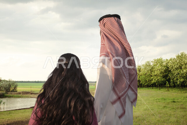 صورة من الخلف لاب وابنته عربيان خليجيان سعوديان يقضيان اوقات ممتعة في احدى الحدائق العامة، نزهه في الهواء الطلق، جولة في الطبيعة الخضراء، انشطة ترفيهية عائلية