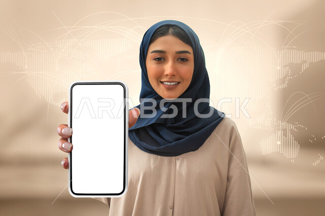 استخدام التقنية في التسويق الرقمي والالكرتوني، تطبيقات الهاتف الذكي، امرأة سعودية خليجية عربية تمسك هاتف محمول بشاشة بيضاء فارغة، اعلانات تسويقية ترويجية، بالونات الهواء الساخنة، خلفلية شبكية لخريطة العالم