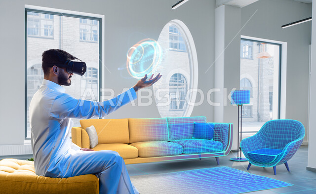 امساك واحتواء عنصر هولوجرامي، رجل عربي خليجي سعودي يرتدي نظارات الواقع الافتراضي ثلاثية الابعاد ويجلس على الاريكة، الاستمتاع والتفاعل ومحاكاة العالم الافتراضي، حركة يد واشارات، ديكورات وتصاميم منزلية