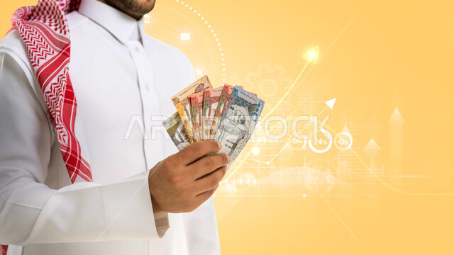 بورتريه لرجل عربي خليجي سعودي يحمل بيده كومة من العملات الورقية، إدخار وتوفير الاموال، عملات نقدية ورقية للريال السعودي، النمو والأرباح المالية، صعود وخبوط مؤشر اقتصادي هولوجرامي، خلفية صفراء